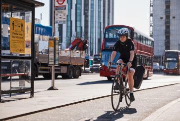 一名妇女在伦敦的自行车道上骑自行车。红色的公共汽车出现在背景中。