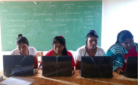 四个女人并排坐在一张桌子前，看着她们的电脑。