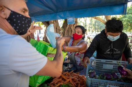 在阿根廷罗萨里奥的农贸市场上，一名妇女递给一名男子新鲜的农产品。